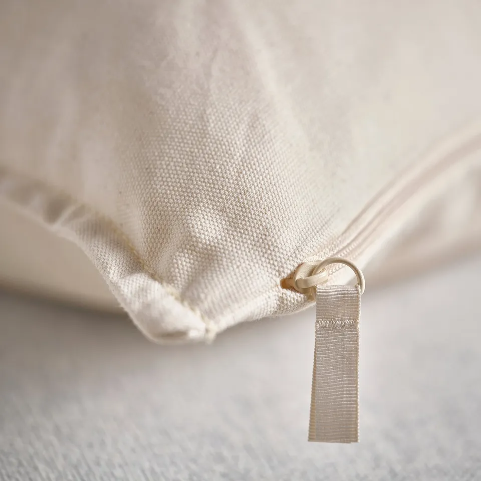 Close-up of zip on white cotton cushion cover, showcasing texture and recycled material quality.