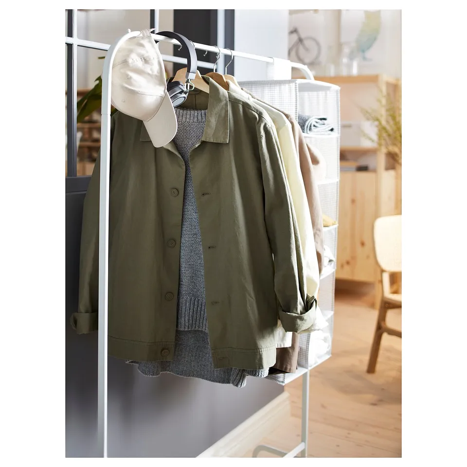 A white MULIG garment rack with green jacket, grey sweater, and beige cap hangs by a mirror.