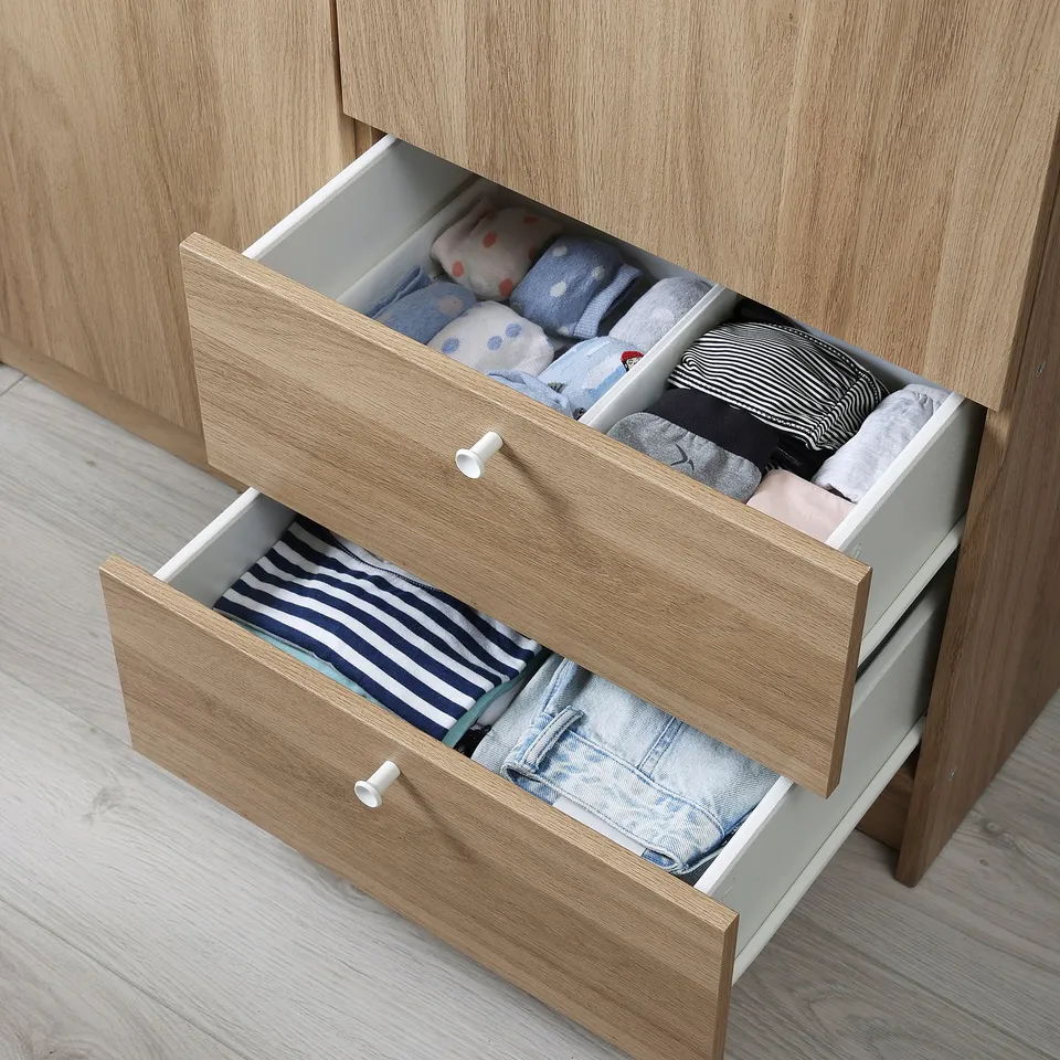 Wooden wardrobe with open drawers filled with neatly folded clothes.