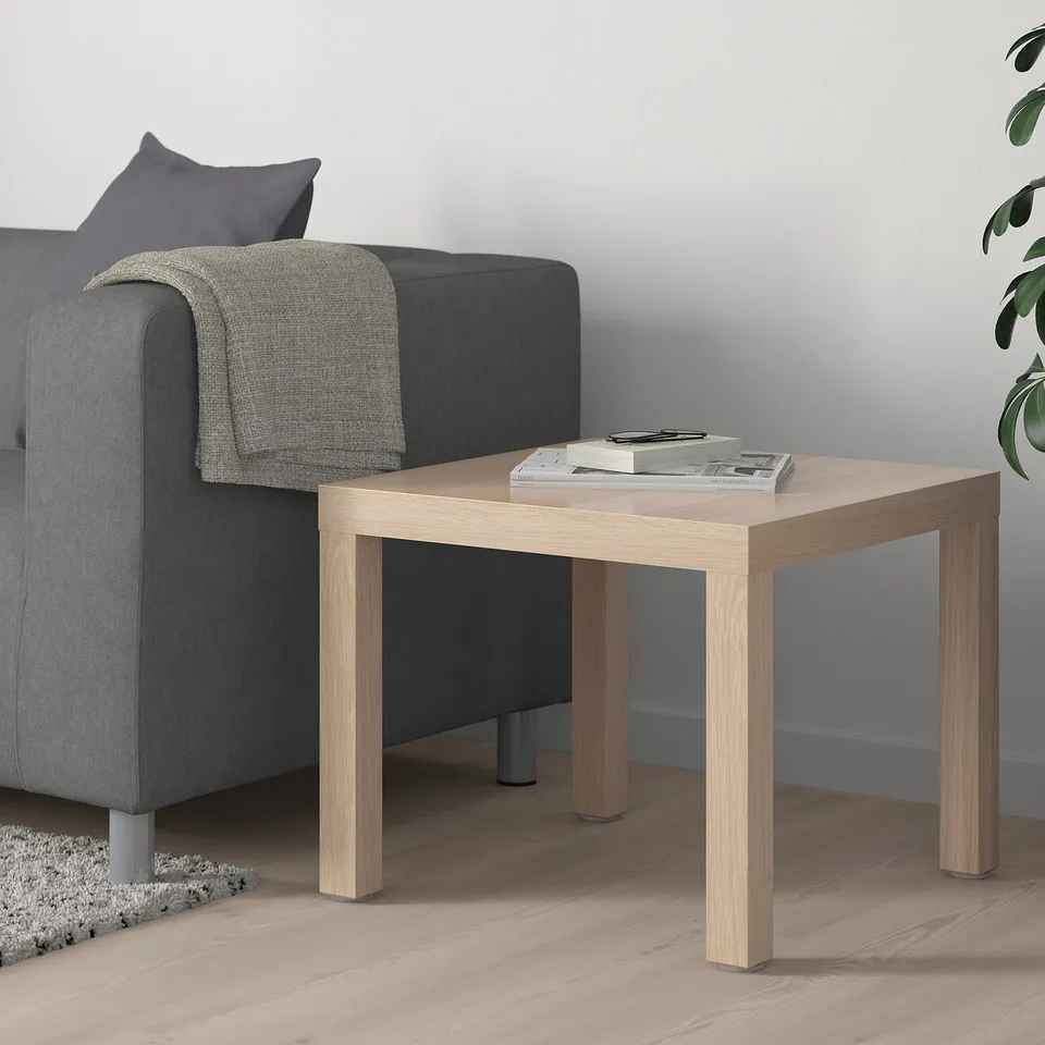 Wooden LACK side table with magazines beside grey sofa, modern design.