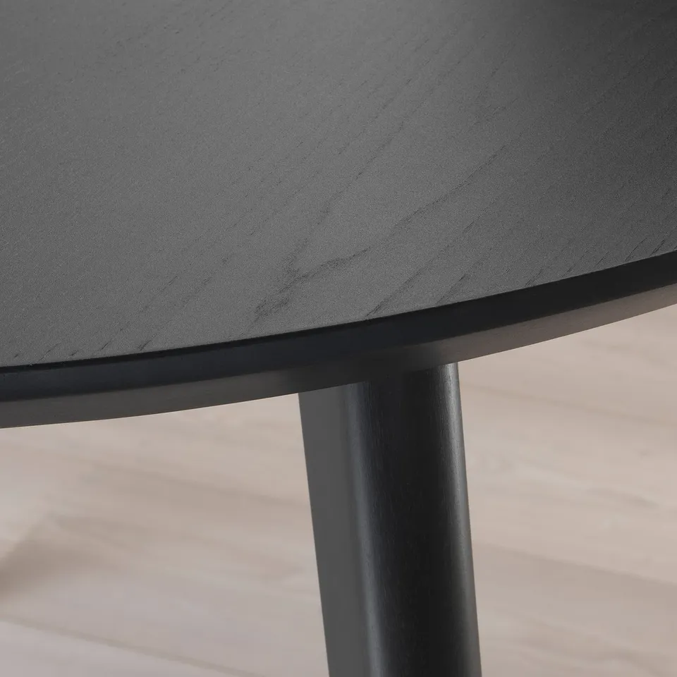 Round dining table close-up: dark, smooth wooden surface and sturdy leg, showcasing high-quality craftsmanship.