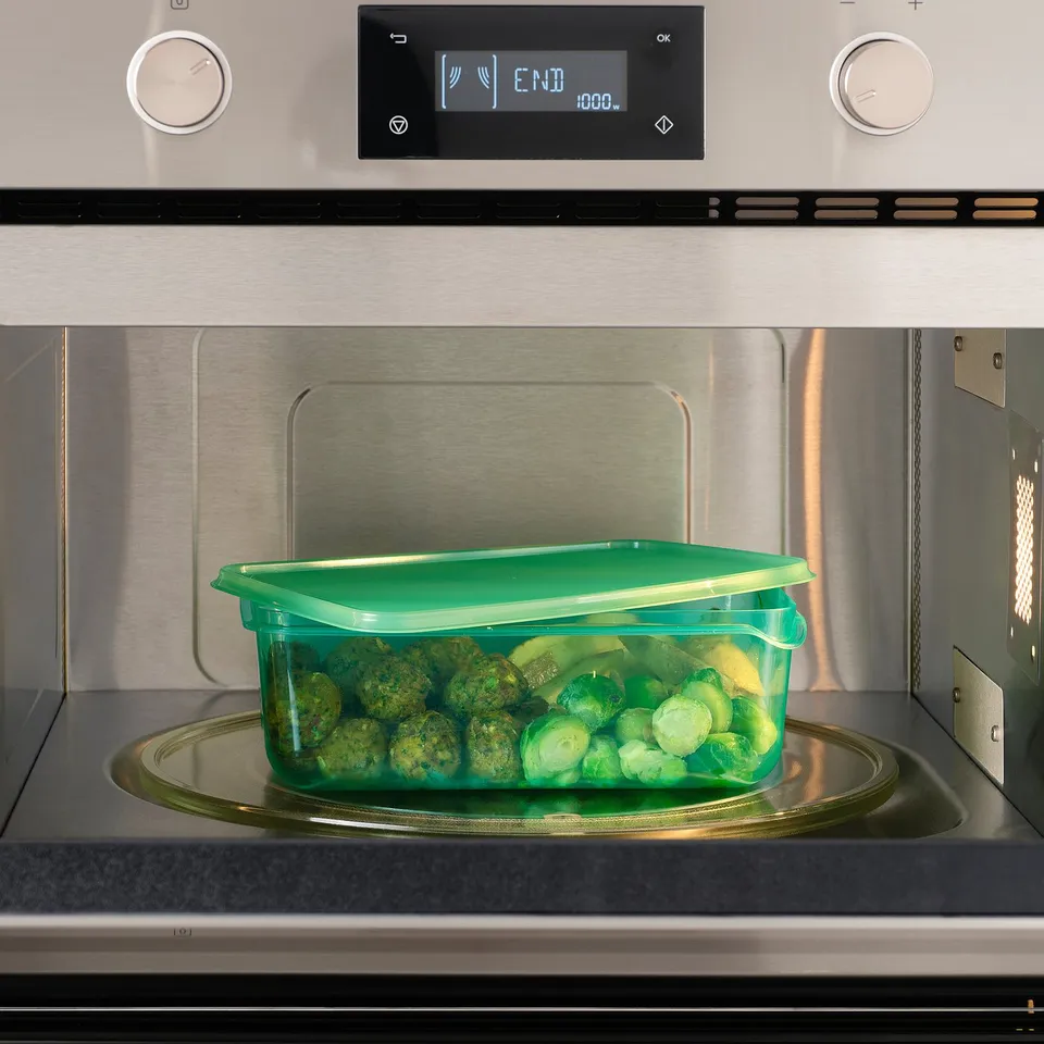 A green plastic container filled with broccoli inside a microwave, demonstrating its use for heating food.