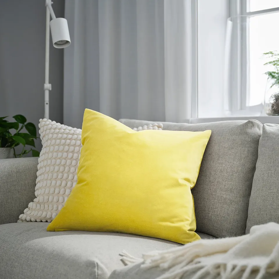 Yellow SANELA pillow, square, on grey couch by window.