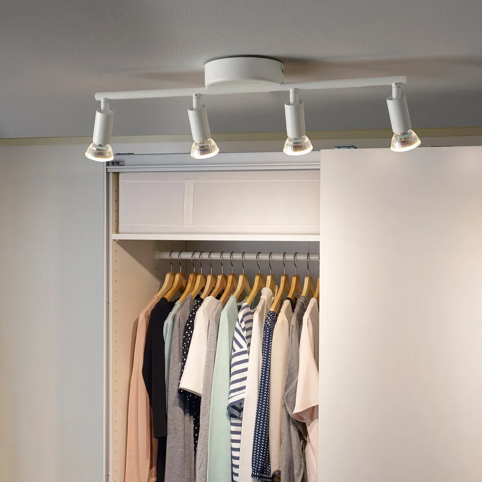 KRUSNATE track lighting holds 4 spots, white. Adjustable lights on a white ceiling, illuminating closet with clothes.