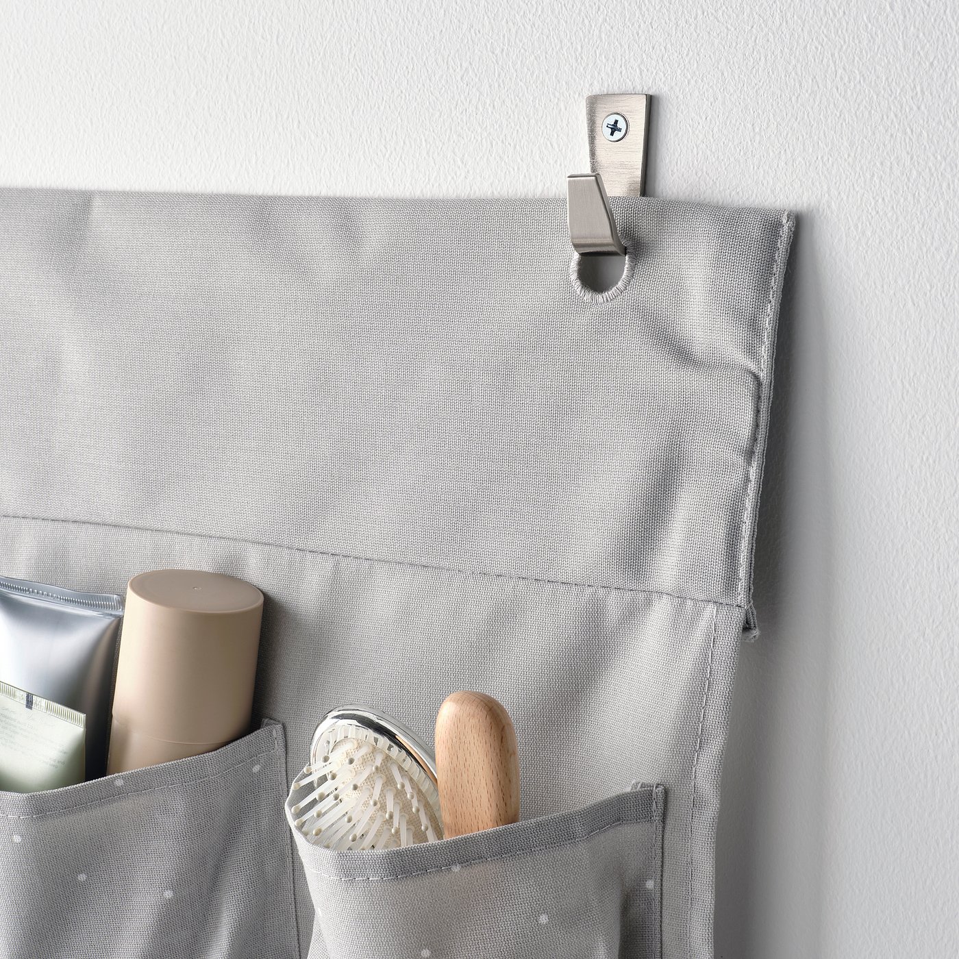 A grey hanging organiser with multiple pockets, holding a bottle, brush, and spatula. Attached to a wall with a metal hook.