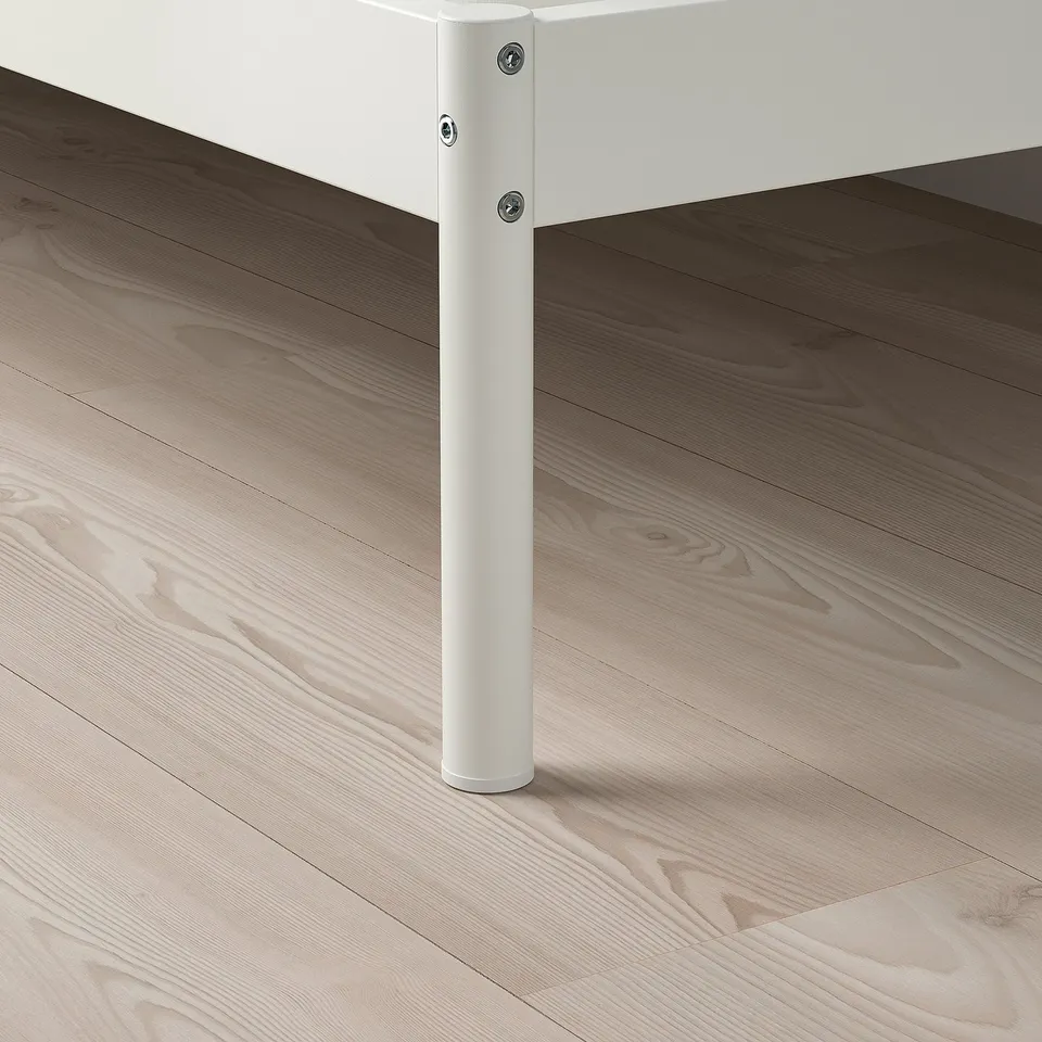 A modern white metal bed leg securely fastened, showing detailed screws and a clean finish, placed on a wooden floor.
