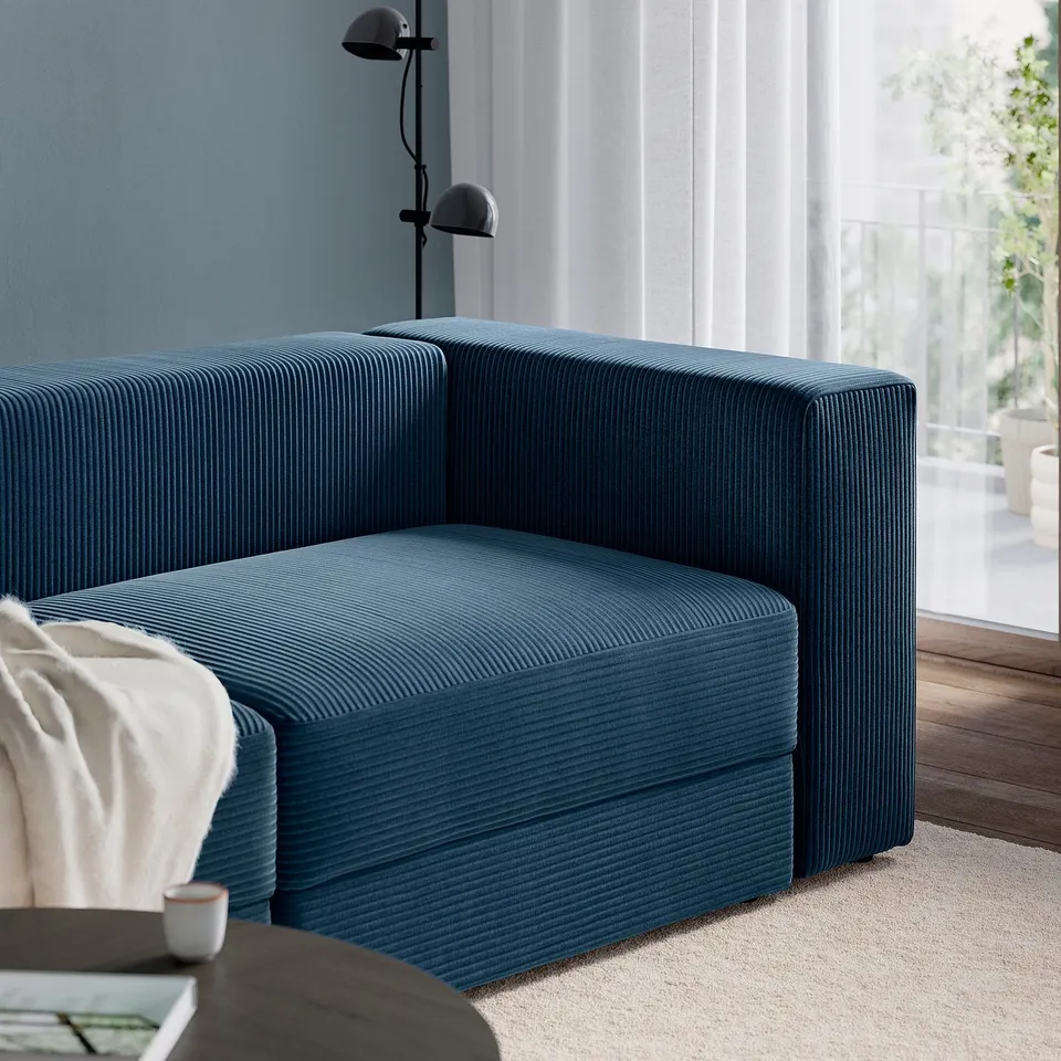 Blue corduroy sofa with white blanket near window.