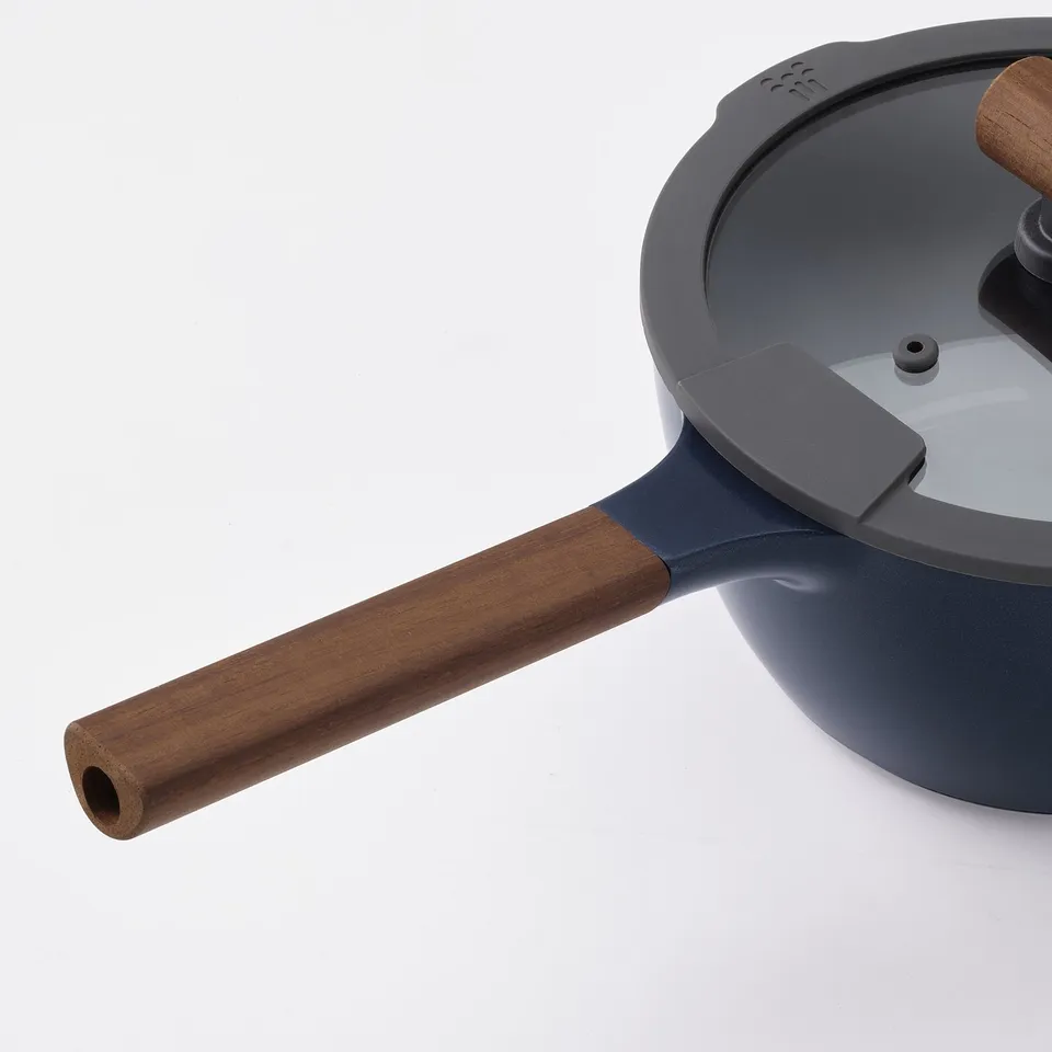 Modern saucepan with dark blue body, wooden handles, and glass lid. High-quality, even heat distribution, non-stick interior.