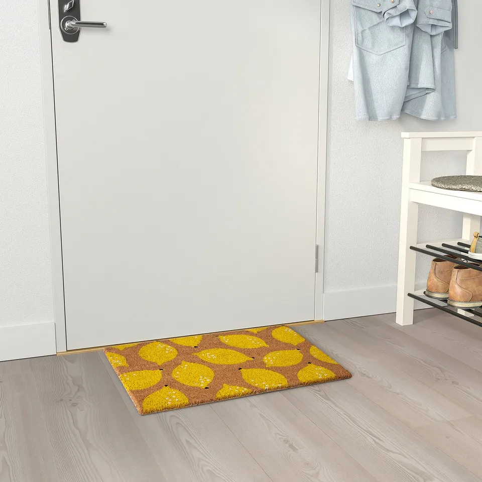 Yellow lemon doormat near white door, cheerful entrance with shoe rack and jacket.