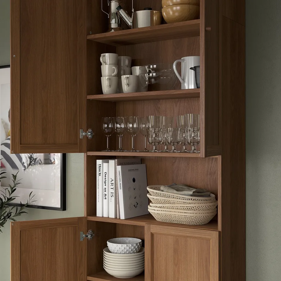 Wooden kitchen cabinet with open shelves, displaying mugs, glasses, bowls, and books. Adjustable shelves allow customizable storage.