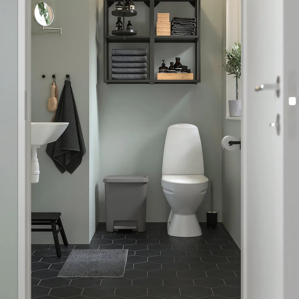 Modern bathroom: white toilet, black hex tiles, green walls & KNÖCKLA bin.