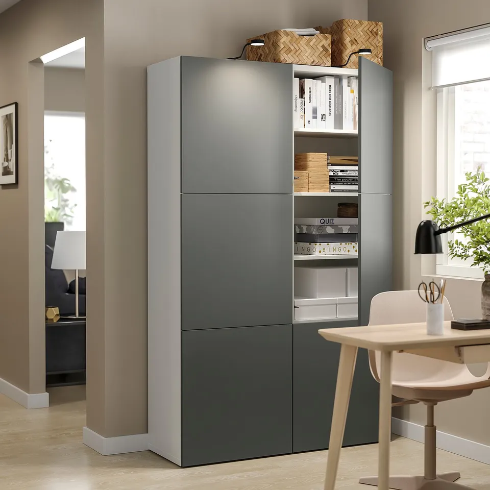 Modern grey BESTÅ storage unit with open and closed compartments, wooden chair, lamp, and books.