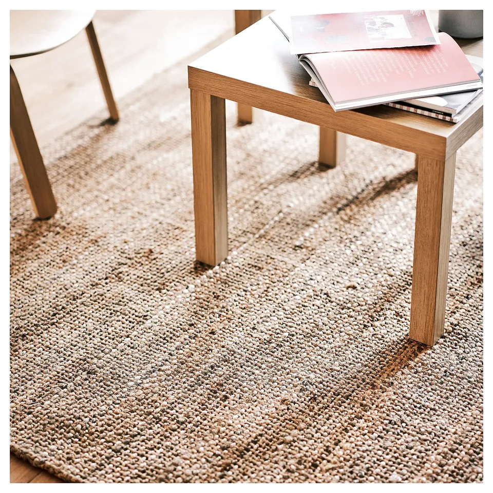 A modern room with a natural jute area rug, light wooden furniture, and books, showcasing a minimalistic design.