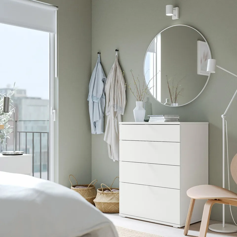 Minimalist bedroom with white VIHALS chest, mirror, stool, wall hooks, baskets, and large window for natural light.