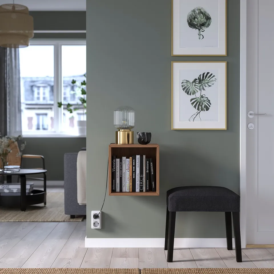 Modern living room with grey walls, black stool, EKET shelf with books and decor, between window and door, under botanical prints.