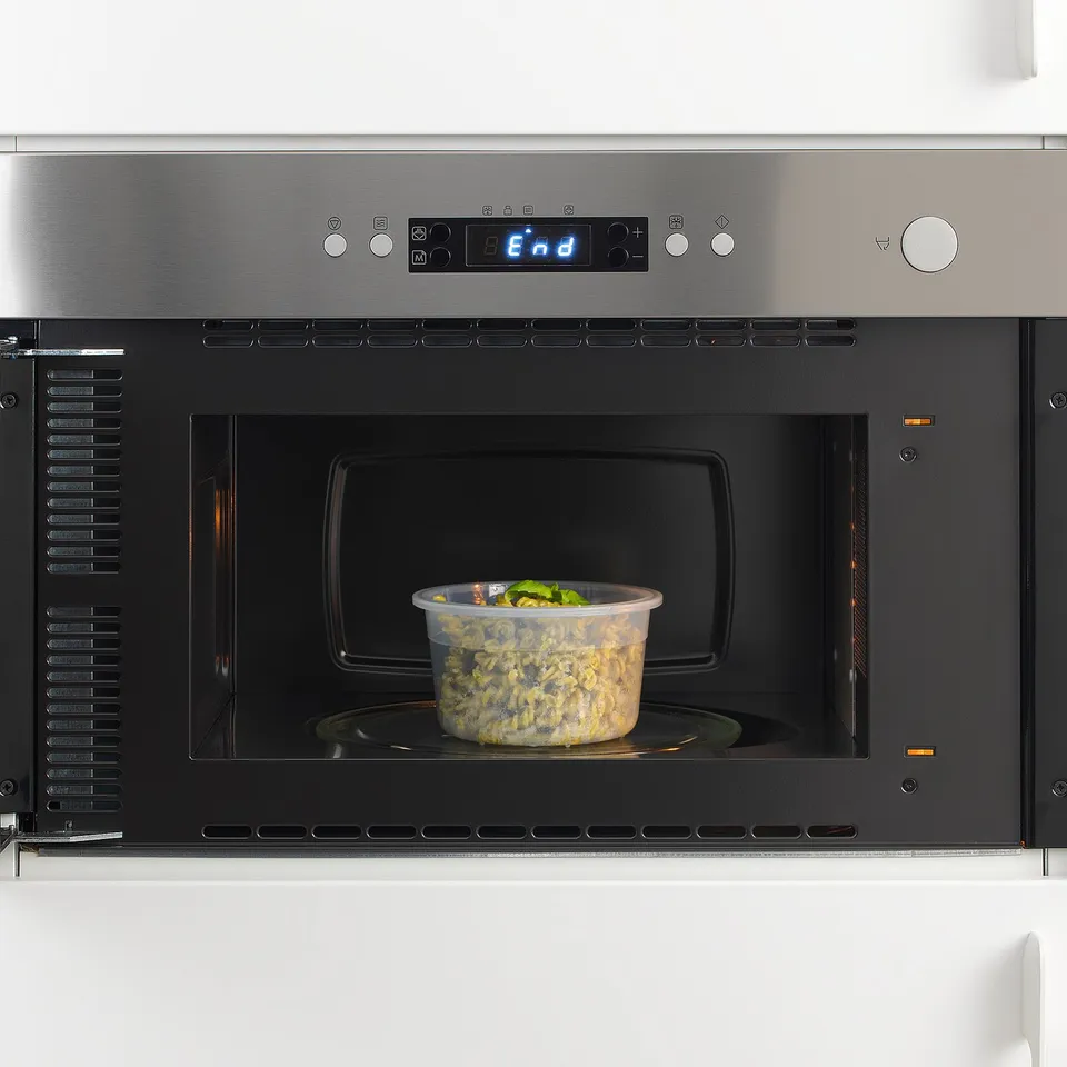 Modern microwave with digital display, heating clear container of food.