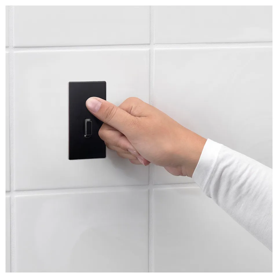 Hand turns black wall switch. White tiled background.