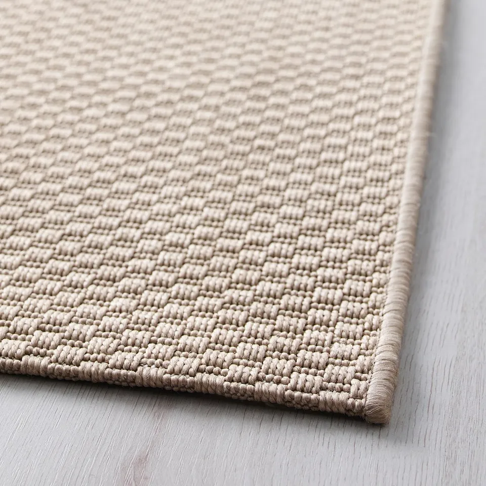 Beige textured rug close-up, showcasing its woven design and edging detail.