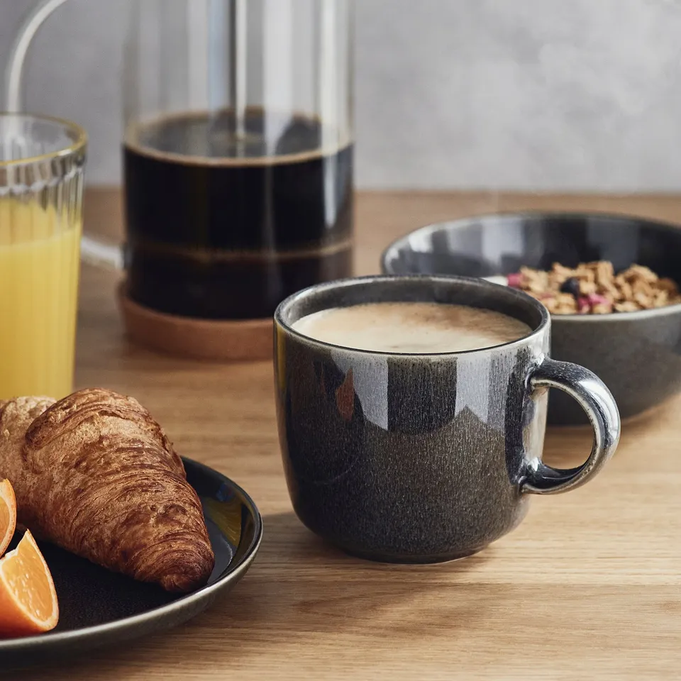 Breakfast setup: coffee, croissant, orange juice, granola. Mug has reactive glaze.