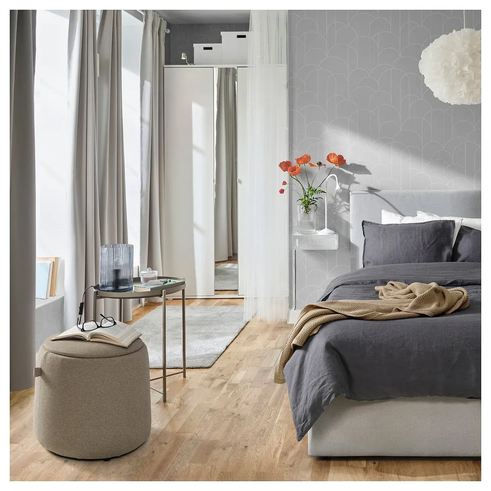 Modern bedroom with a JÄRRESTAD pouffe, grey, round, wooden floors, grey bedding, grey curtains, and a grey rug.