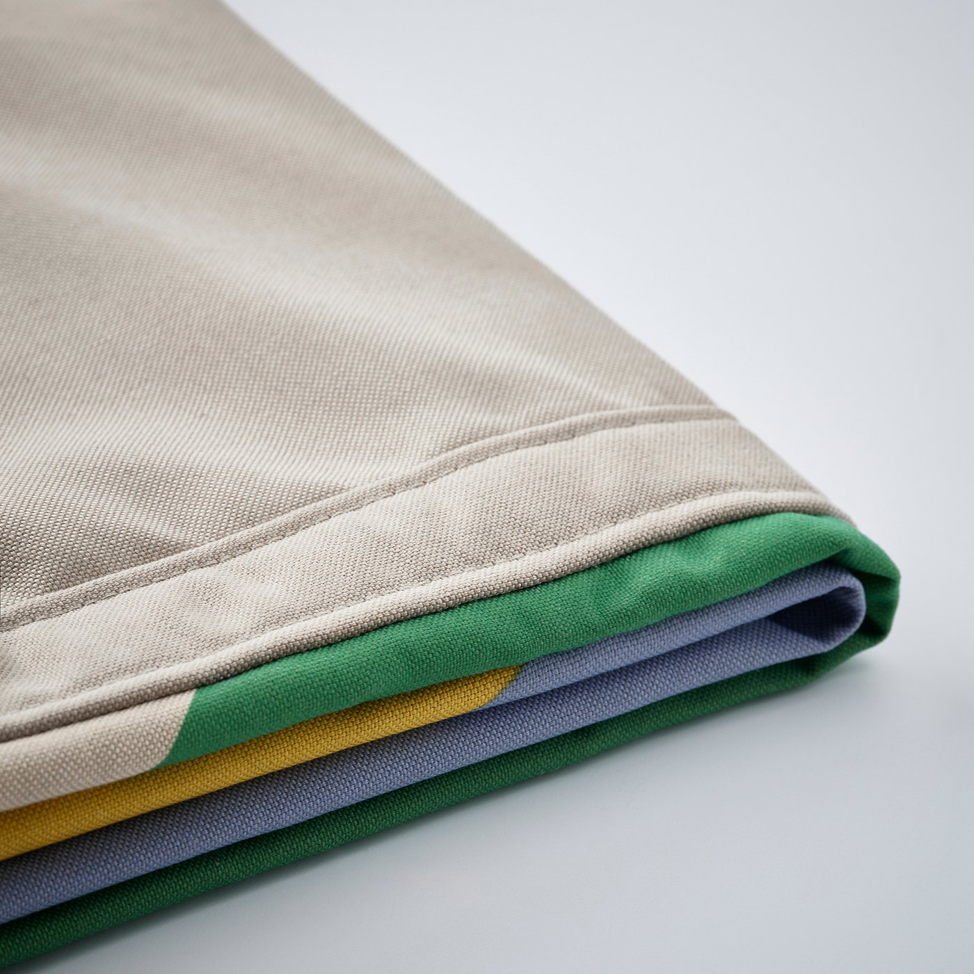 Folded fabric in beige, green, grey, and yellow, showcasing quality texture and stitching.