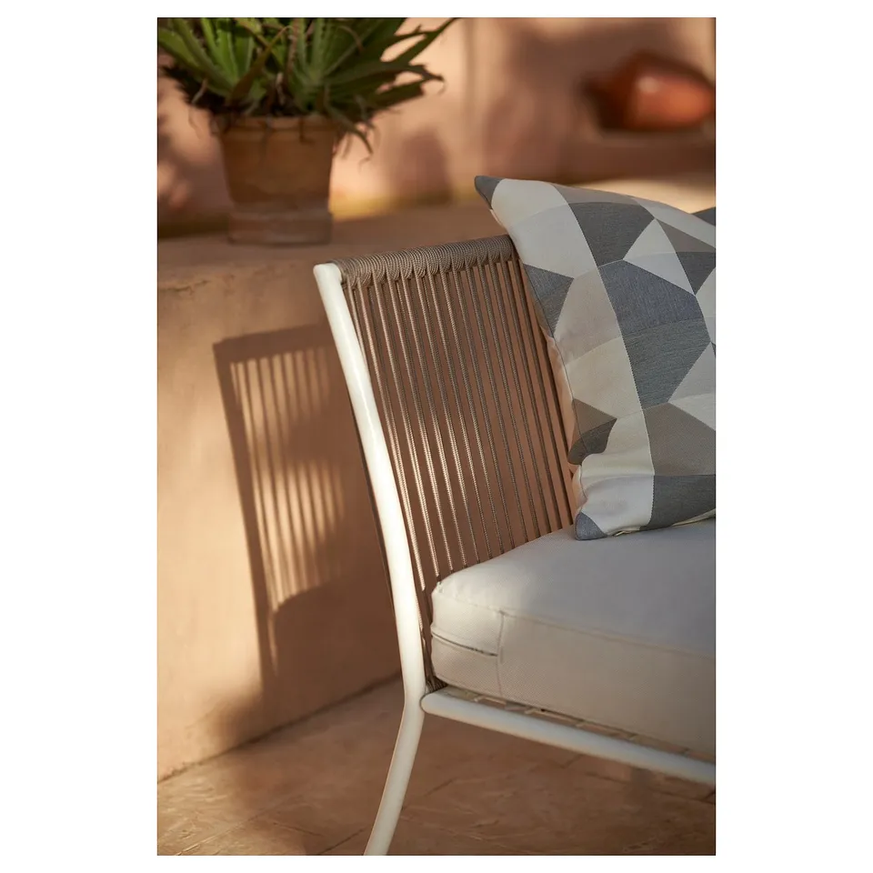 Modern outdoor chair with geometric pillow, white frame, seated on terrace.