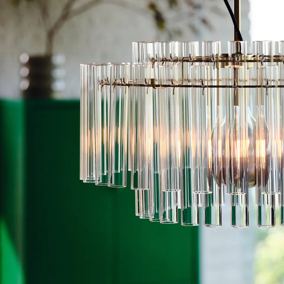 A modern chandelier with 54 glass cylinders hangs from a brass-plated hook. It provides direct light, suitable for a dining table or living room.