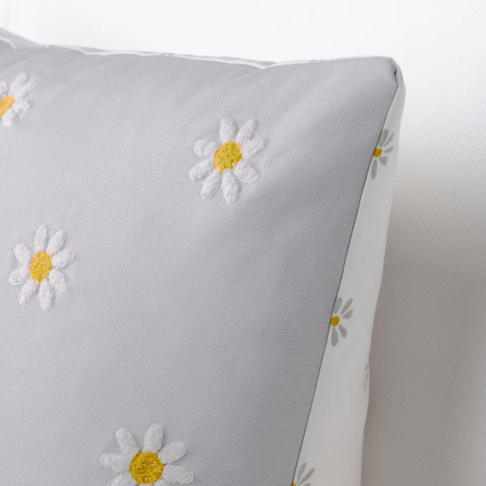 A close-up of white cushion with yellow and white daisies, soft cotton fabric, embroidered details.