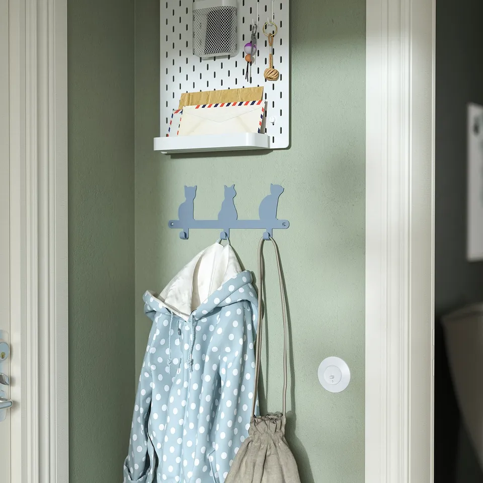 A wall-mounted cat-shaped hook rack holding a childs polka dot jacket and bag, with additional storage above for small items.