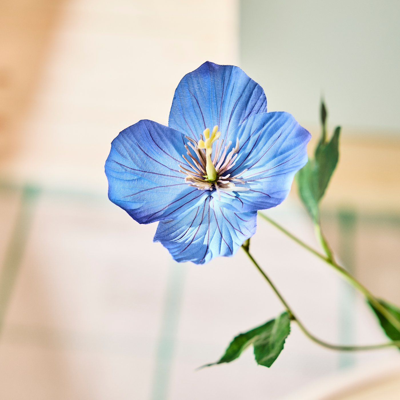 Bright blue artificial flower, vivid petals surrounding a yellow centre, attached to green stem with leaves.