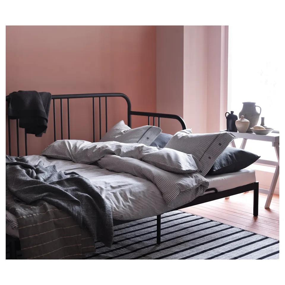 Modern black metal day-bed with striped bedding, against pink walls. Minimalist and stylish guest bed.