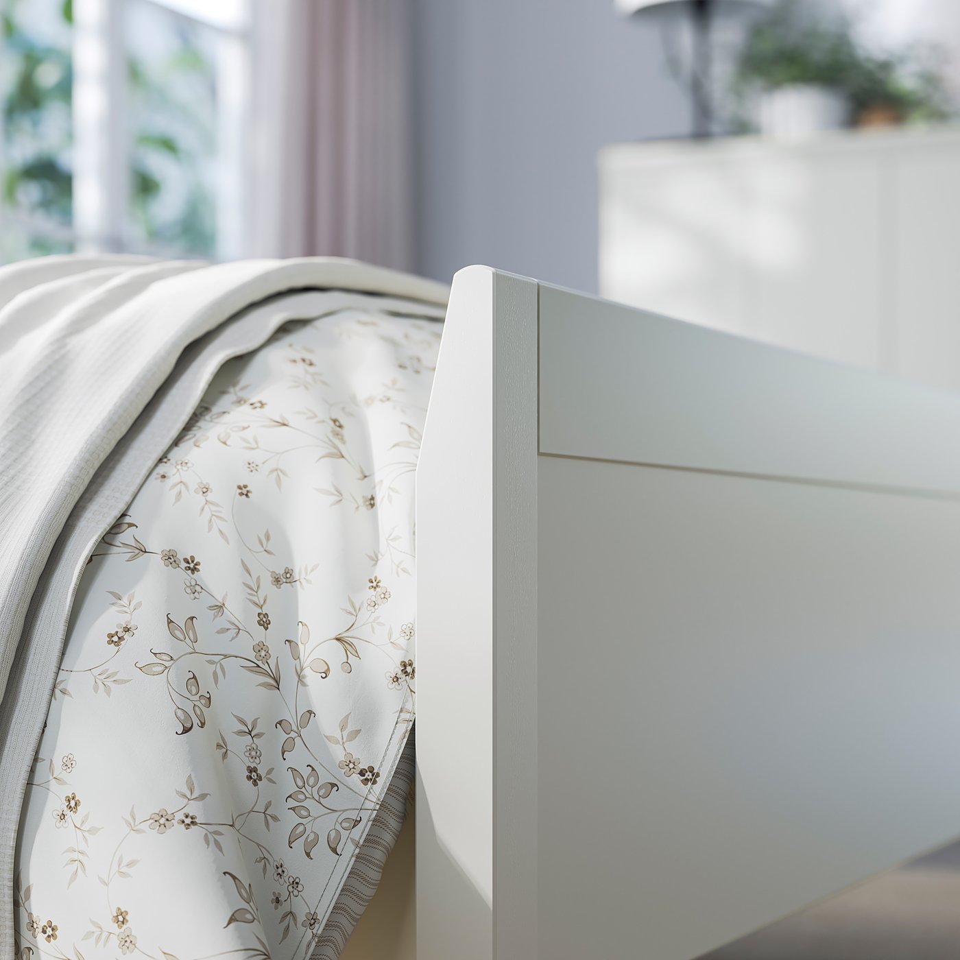 A white IDANÄS bed with a classic headboard, flowery bedsheet, and light blue curtains.