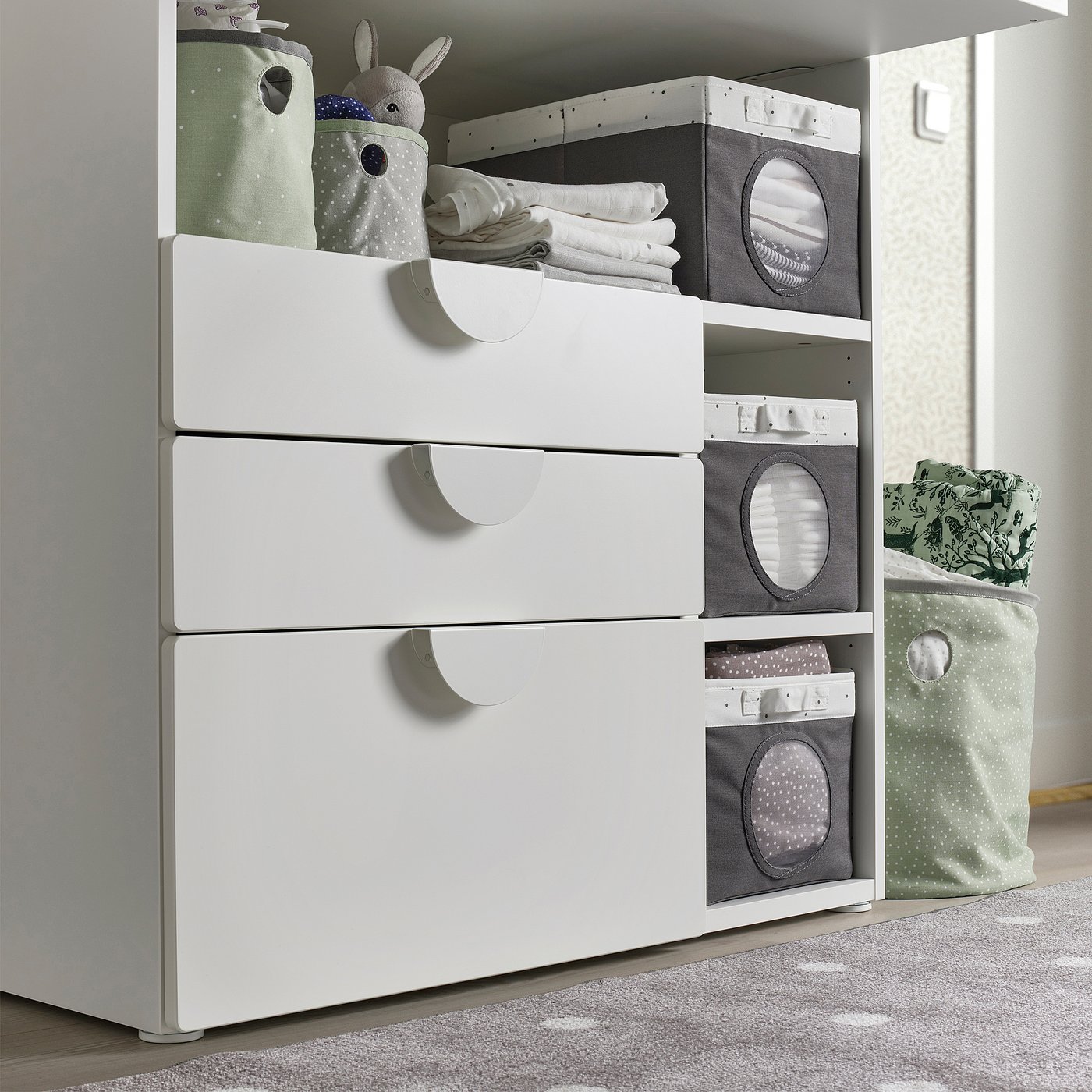 White storage unit with drawers and grey fabric storage bins, used for organising baby items like clothes and toys. Suitable for ages 3+ years.