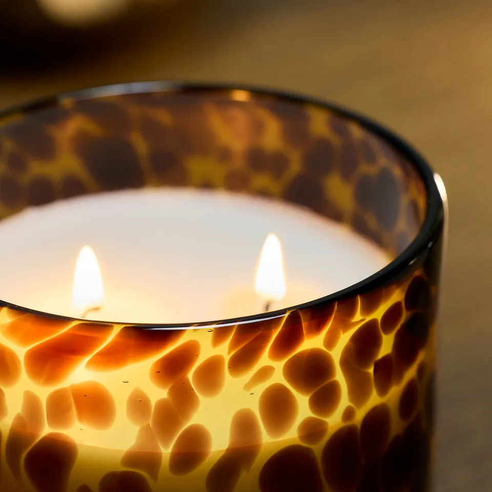 A multi-wick scented candle in a hand-blown glass container with a leopard print pattern, emitting a warm, inviting glow.