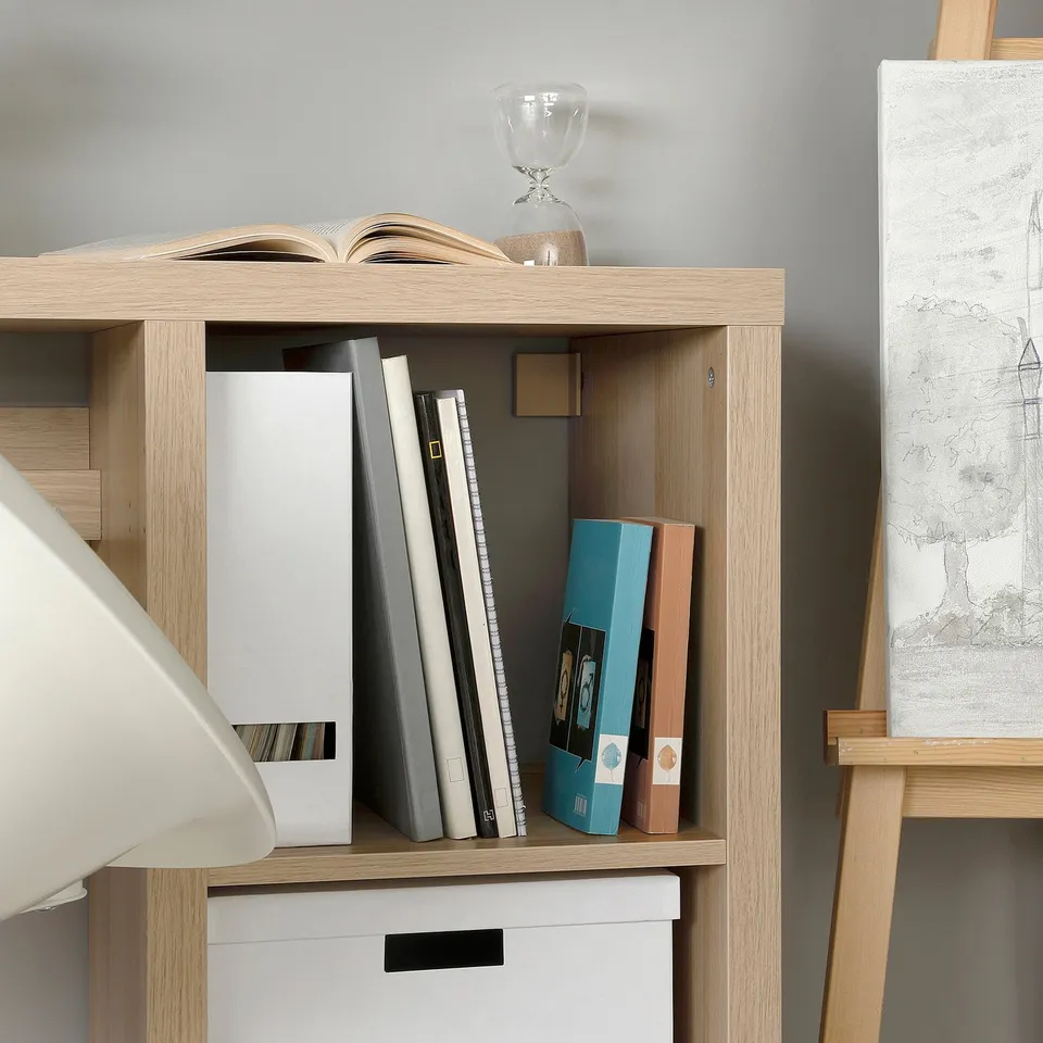 Wooden shelving unit with multiple compartments, neatly storing books, binders, and an artists drawing.