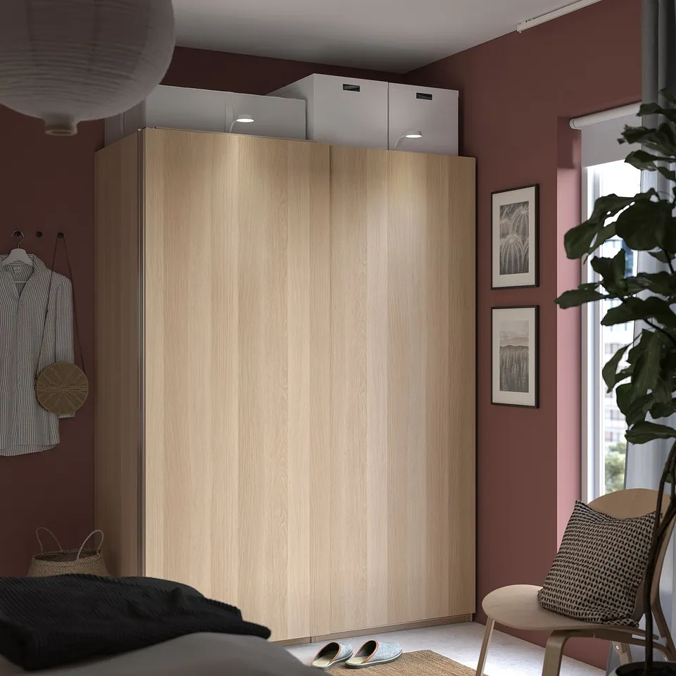 Modern bedroom with red walls and light wood pax wardrobe, sliding door, shirt, lantern, and chair.
