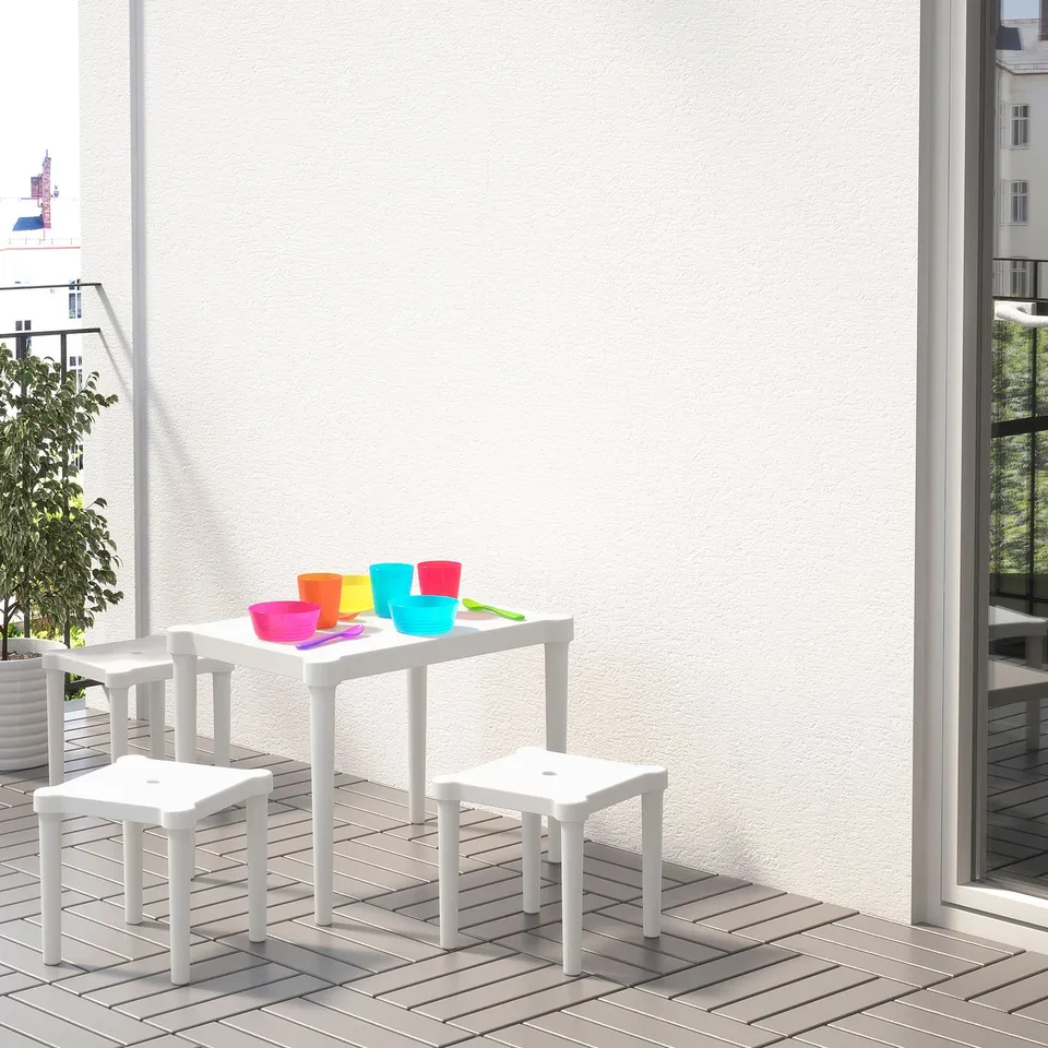Small childrens play area with a white plastic table and chairs. Colourful cups and spoons on the table, suitable for arts, crafts, or snack time.