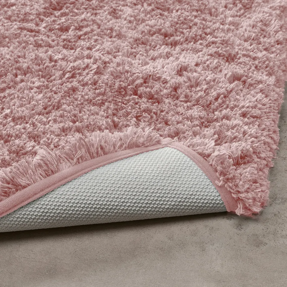 Pink plush bath mat with white textured non-slip backing.
