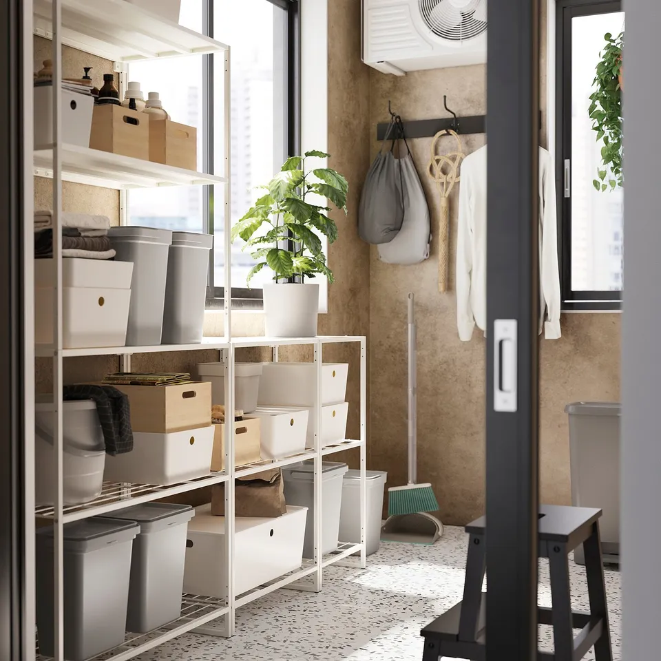 Organised storage room with white JOSTEIN shelves holding boxes, a potted plant, and hanging laundry bags.