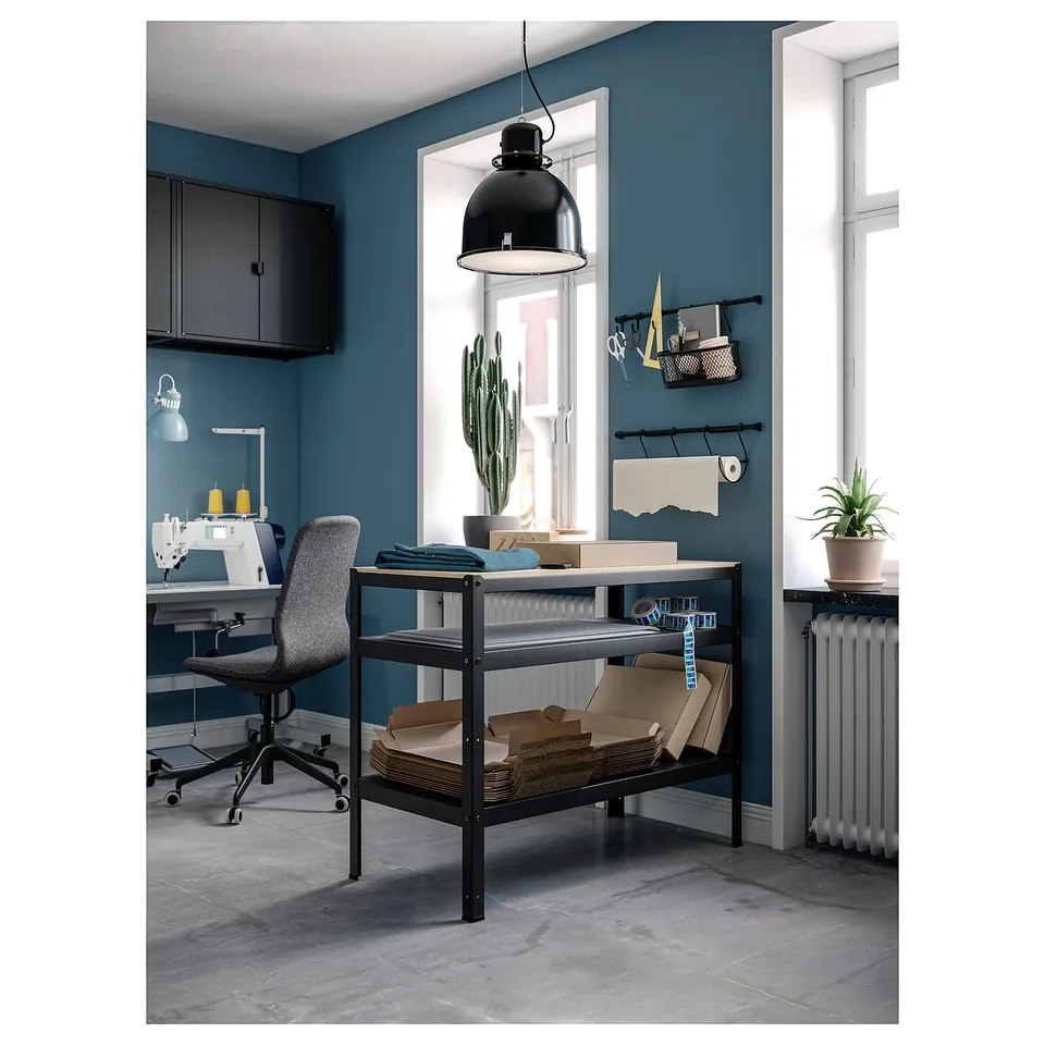 A modern home office with a black metal desk and chair, blue walls, and a large window. A hanging lamp, storage shelves, and a cactus plant.