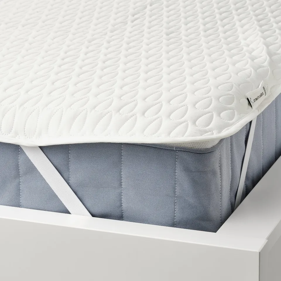 White mattress protector with waffle pattern. Elastic straps secure it on the mattress. Protects from liquid spills and stains.