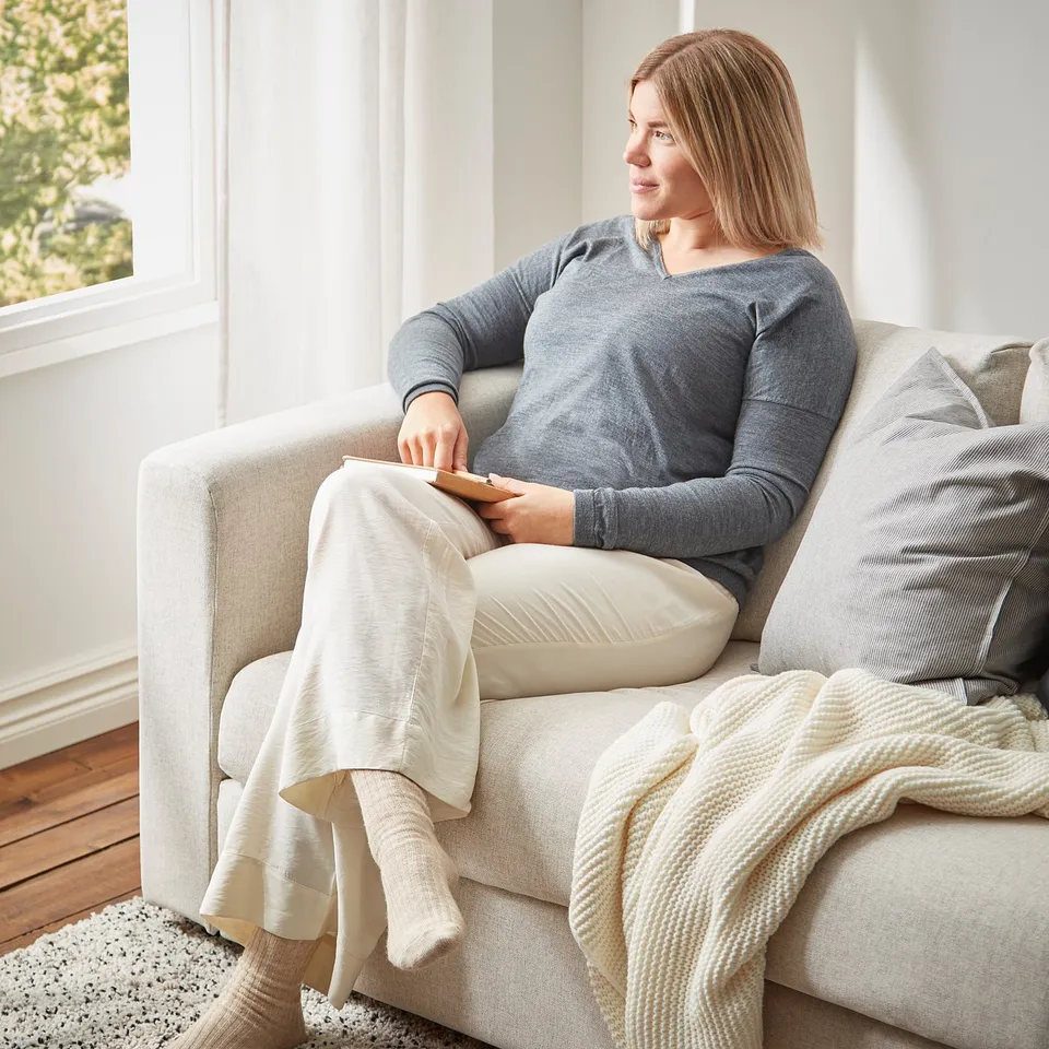 Person relaxes on VIMLE sofa, grey, cosy, soft cushions, cream throw blanket, natural light.