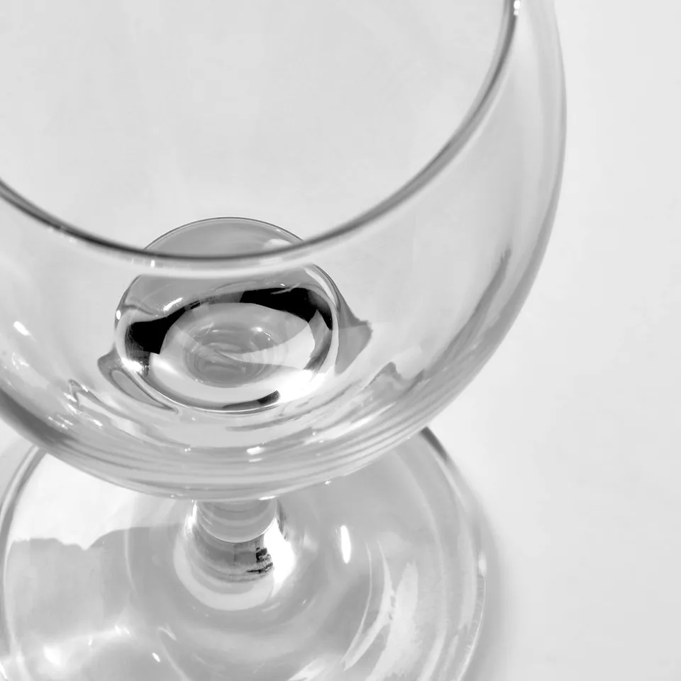 Close-up of clear, empty wine glass with long stem, reflecting light, showing transparency and quality.