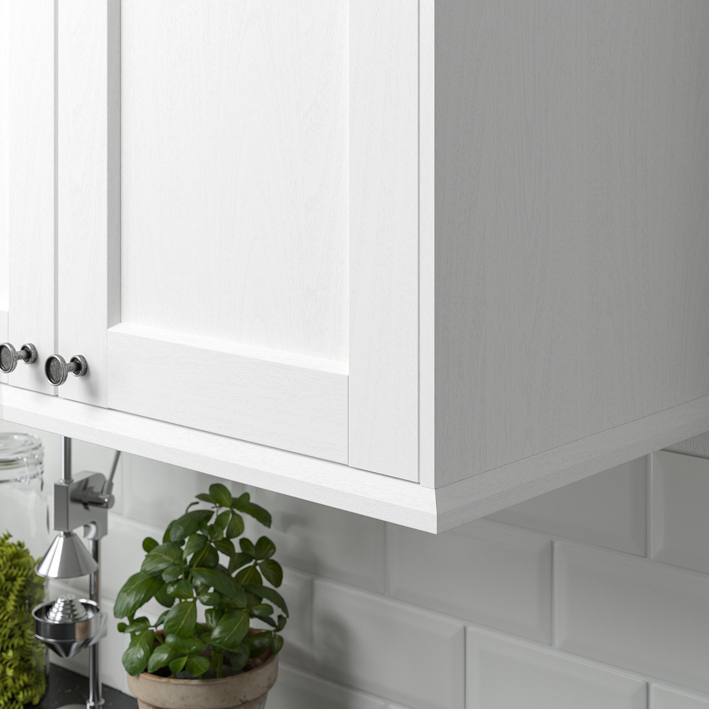 White kitchen cabinet with ENKÖPING trim, covering lighting and cords, plant on counter.