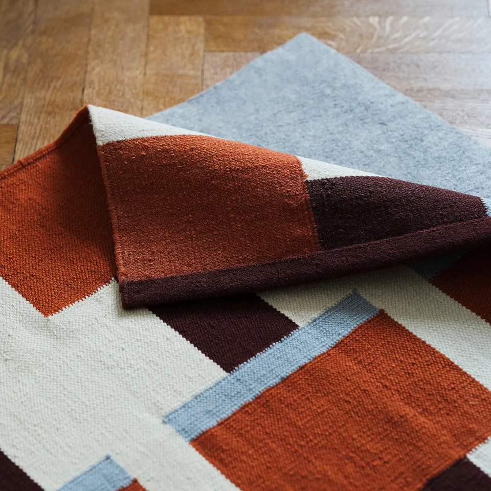 Reversible wool rug with geometric patterns in orange, brown, white, and blue on wooden floor.