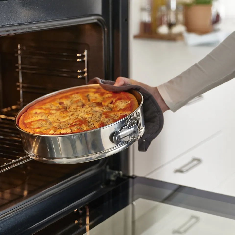 Person removes deep-dish pizza from oven using a springform pan. The ovens heat distributes evenly for perfect baking.