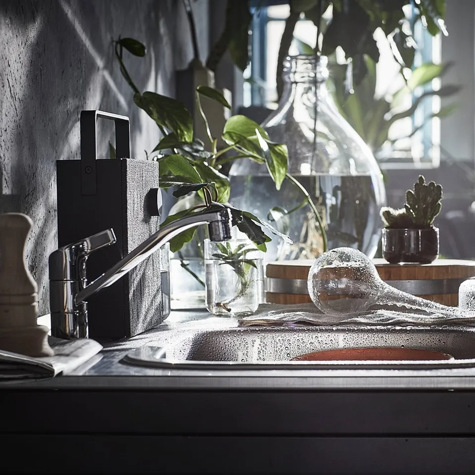 Black kitchen sink with silver tap, plants, and glassware.