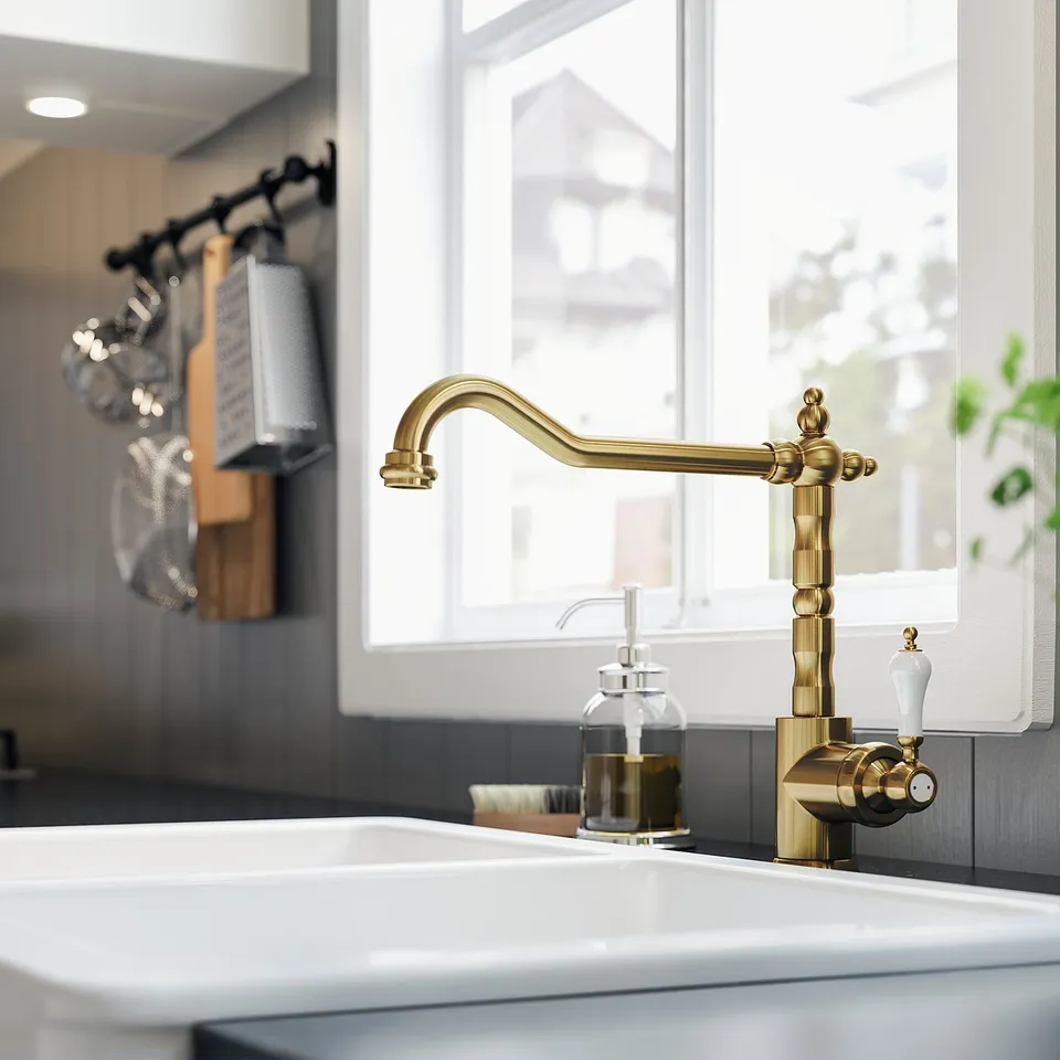 Antique brass kitchen tap with white handles near window.