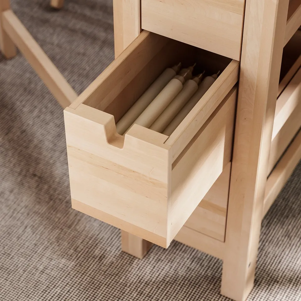 Light wooden table with one open drawer revealing cylindrical items.