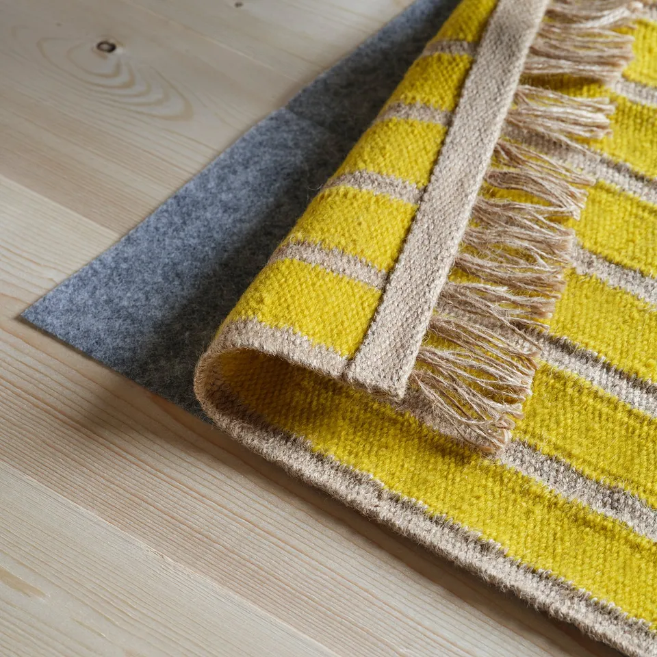 Yellow striped rug with fringes, handwoven from jute and wool, perfect for warm, decorative floors.